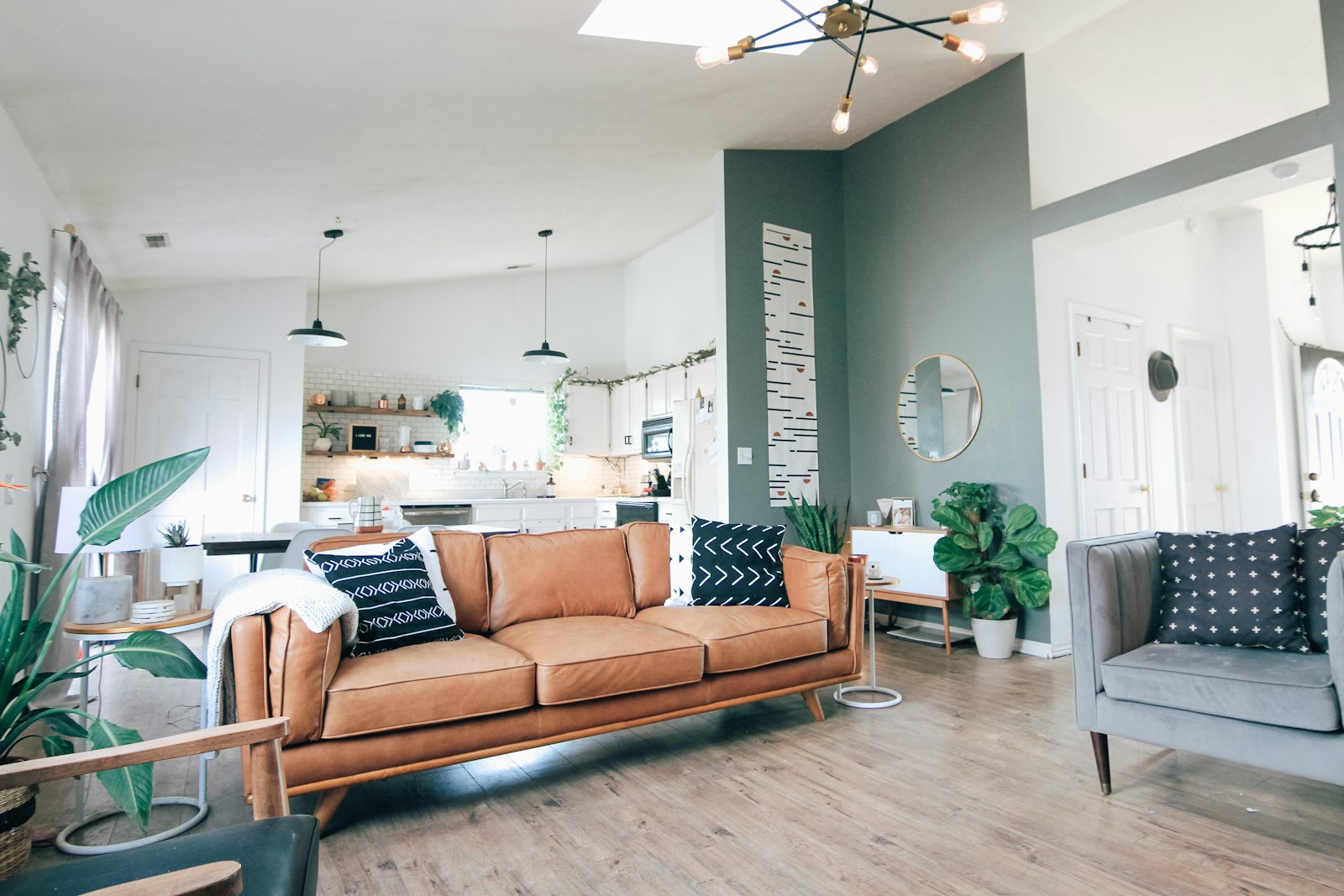 Warm living room lit by an Edison-bulb chandelier and two pendant lamps, with a wall light switch visible on the teal accent wall - the smart switch vs smart bulb decision in a real home