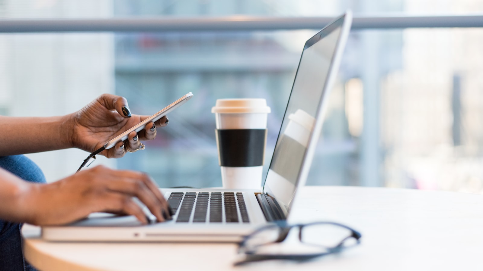 A person holding a phone with a smart home control app open next to a MacBook in a warm interior